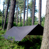 DD Tarp XL set up between trees in a forest, providing shelter for campers and outdoor enthusiasts.